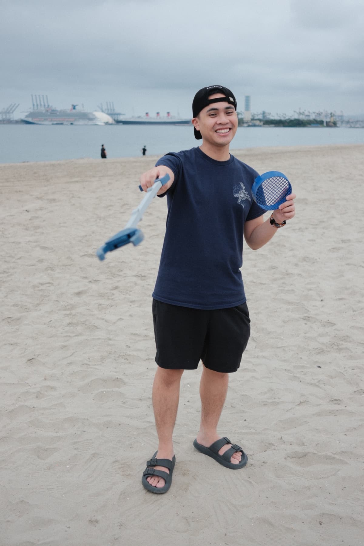 Founder holding a 3D-printed cleanup tool on the beach during First Wave.